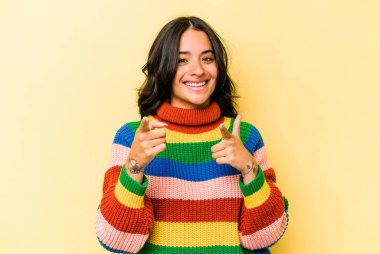 Sarı arka planda izole edilmiş genç İspanyol kadın parmaklarıyla ön tarafı işaret ediyor..