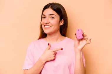 Latin kökenli genç bir kadın, elinde bej arka planda izole edilmiş bir araba tutuyor gülümsüyor ve boş alanda bir şeyler gösteriyor..