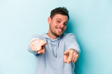 Mavi arka planda izole edilmiş genç beyaz adam parmaklarıyla ön tarafı işaret ediyor..