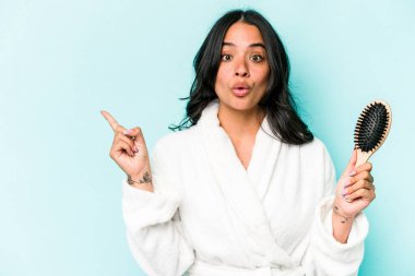 Mavi arka planda saç fırçası tutan genç İspanyol kadın yan tarafı işaret ediyor.