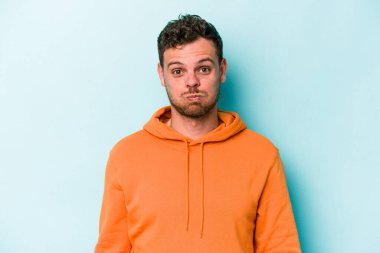 Mavi arka planda izole edilmiş genç beyaz adamın yanakları şişer, yorgun bir ifadesi vardır. Yüz ifadesi kavramı.