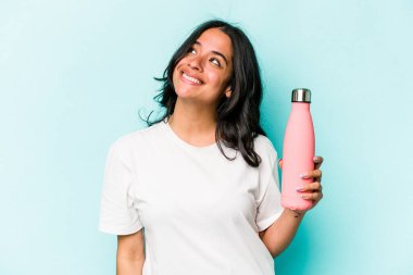 Mavi arka planda termo tutan genç İspanyol kadın hedeflerine ve amaçlarına ulaşma hayali kuruyor.