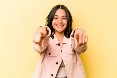 Sarı arka planda izole edilmiş genç İspanyol kadın. Önü işaret eden neşeli gülümsemeler..