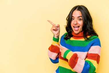 Sarı arka planda izole edilmiş genç İspanyol kadın işaret parmaklarıyla fotokopi alanını işaret ederek heyecan ve arzusunu ifade ediyor..