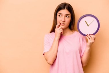Latin kökenli genç bir kadın bej arka planda izole edilmiş bir saat tutuyor rahatlamış bir şeyin fotokopi odasına baktığını düşünüyor..