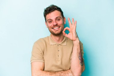 Kafkasyalı genç bir adam mavi arka planda izole edilmiş bir şekilde göz açıp kapayana kadar iyi bir el hareketi yapıyor..