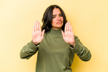 Sarı arka planda izole edilmiş genç İspanyol kadın elini uzatmış, dur işareti göstererek seni engelliyor..