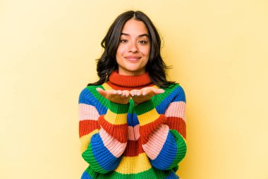 Sarı arka planda izole edilmiş genç İspanyol kadın elinde avuç içi bir şeyle kameraya sunuyor..