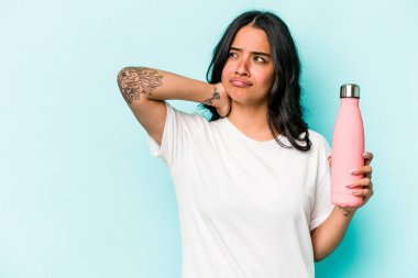 Termosu mavi arka planda tutan genç İspanyol kadın kafasının arkasına dokunuyor, düşünüyor ve bir seçim yapıyor..