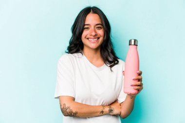 Mavi arka planda termo tutan genç İspanyol kadın gülüyor ve eğleniyor..