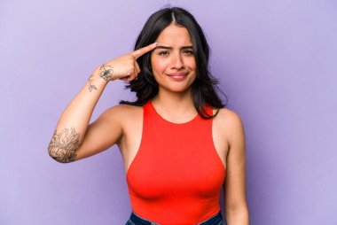 Mor arka planda izole edilmiş genç İspanyol bir kadın şakağı parmağıyla işaret ediyor, düşünüyor ve bir göreve odaklanıyor..
