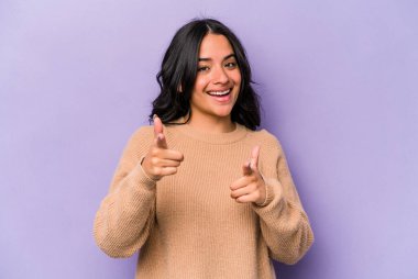 Mor arka planda izole edilmiş genç İspanyol kadın parmaklarıyla ön tarafı işaret ediyor..