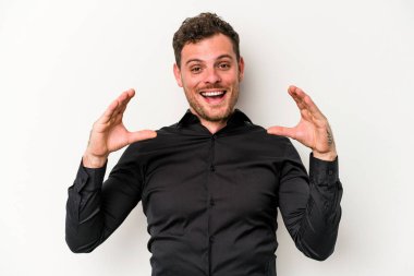 Beyaz arka planda izole edilmiş genç beyaz bir adam elinde avuç içi bir şeyle kameraya sunuyor..