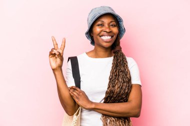 Genç Afrikalı Amerikalı bir kadın pembe arka planda izole edilmiş plaja gidiyor. İki numarayı parmaklarıyla gösteriyor..