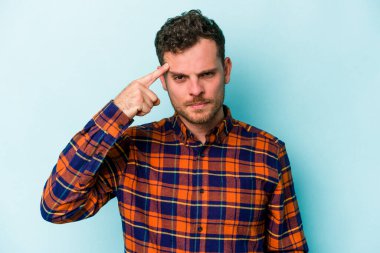Mavi arka planda izole edilmiş genç beyaz bir adam şakağı parmağıyla işaret ediyor, düşünüyor ve bir göreve odaklanıyor..
