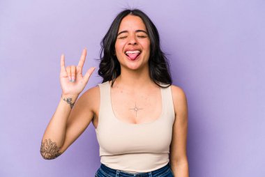 Mor arka planda izole edilmiş genç İspanyol kadın parmaklarıyla taş hareketi gösteriyor.