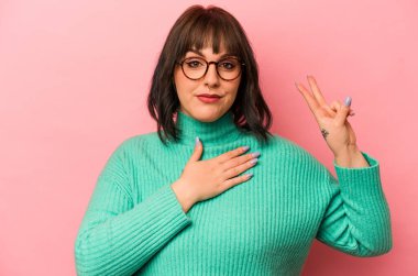 Pembe arka planda izole edilmiş genç beyaz kadın yemin ediyor, elini göğsüne koyuyor..