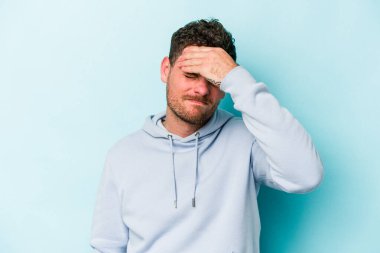 Genç beyaz adam mavi arka planda izole edilmiş tapınaklara dokunuyor ve başı ağrıyor..