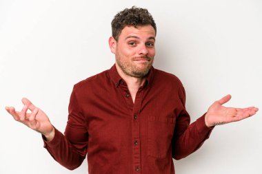 Beyaz arka planda izole edilmiş genç beyaz bir adam sorgulama sırasında omuz silkiyor ve şüphe duyuyor..