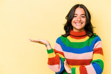 Sarı arka planda izole edilmiş genç İspanyol kadın bir avuç içinde fotokopi alanı ve belinde bir el daha gösteriyor..