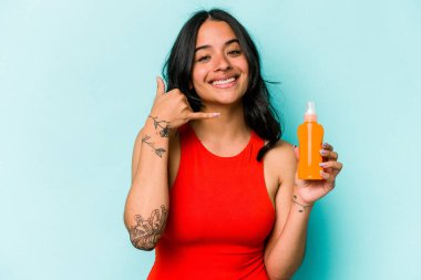 Mavi arka planda güneş kremi tutan genç İspanyol kadın cep telefonu hareketini parmaklarıyla gösteriyor..