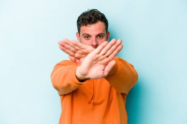 Kafkasyalı genç adam mavi arka planda izole edilmiş bir şekilde inkar hareketi yapıyor.
