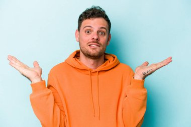 Kafkasyalı genç adam mavi arka planda izole edilmiş. Kafası karışmış ve omuz silkiyor. Kopya alanını tutmak için..