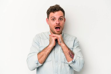 Beyaz arka planda izole edilmiş genç beyaz bir adam şans için dua ediyor, şaşırmış ve ağzını açıp önüne bakıyor..