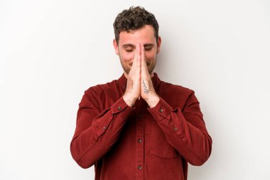 Beyaz arka planda izole edilmiş genç beyaz bir adam el ele tutuşup, ağız kenarında dua ediyor, kendinden emin..