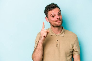 Mavi arka planda izole edilmiş genç beyaz adam bir numarayı parmağıyla gösteriyor..