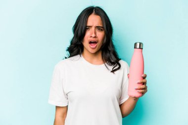 Mavi arka planda termosu olan genç İspanyol kadın çok sinirli ve agresif bağırıyor..