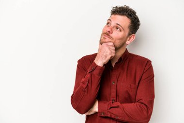 Beyaz arka planda izole edilmiş genç beyaz bir adam şüpheli ve şüpheci bir ifadeyle yana bakıyor..