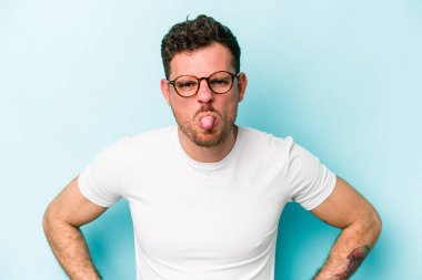 Kafkasyalı genç adam mavi arka planda izole edilmiş komik ve dost canlısı bir dil uzatıyor..