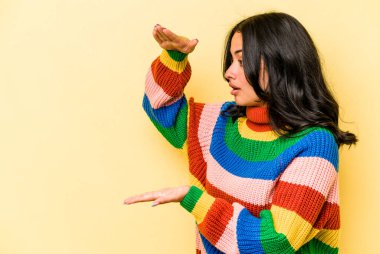 Sarı arka planda izole edilmiş genç İspanyol kadın elleri arasında bir kopya alanı tutarken şok ve hayrete düştü..