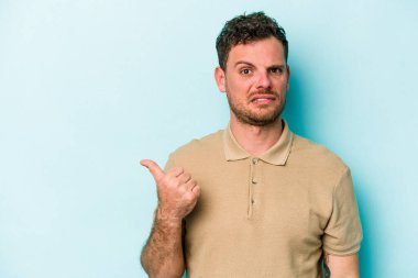 Mavi arka planda izole edilmiş genç beyaz adam işaret parmağıyla fotokopi alanını işaret ederek şok oldu..