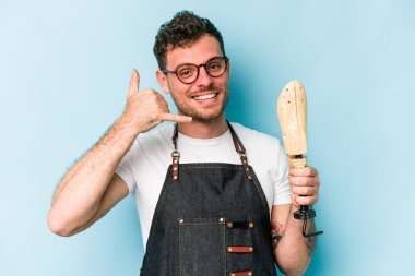 Kafkasyalı genç kunduracı, mavi arka planda izole edilmiş, parmakları olan bir cep telefonu hareketi gösteriyor..