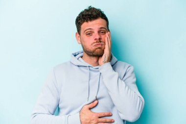 Mavi arka planda izole edilmiş genç beyaz adamın yanakları şişer, yorgun bir ifadesi vardır. Yüz ifadesi kavramı.