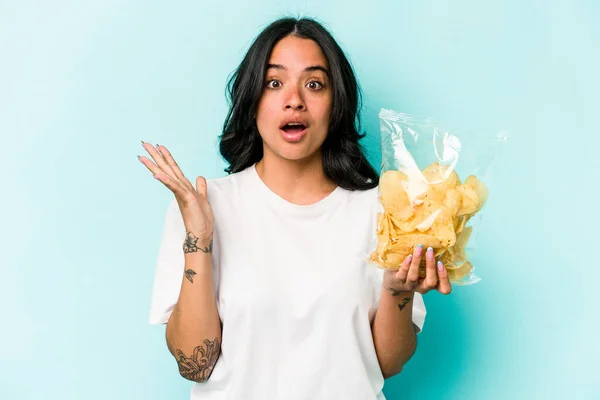 Ung Latinamerikansk Kvinna Håller Påse Chips Isolerad Blå Bakgrund Förvånad — Stockfoto