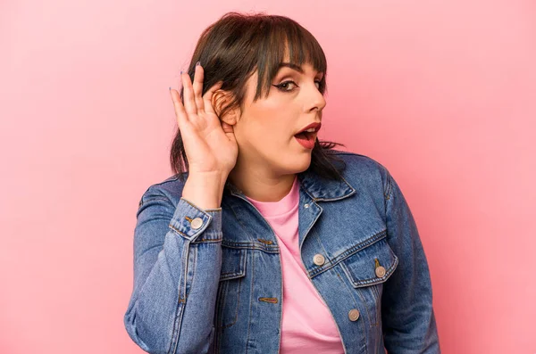 Pembe arka planda izole edilmiş genç beyaz kadın bir dedikoduyu dinlemeye çalışıyor..