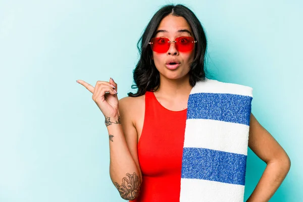 stock image Young hispanic woman holding beach towel isolated on blue background pointing to the side