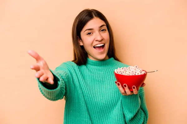 若いですヒスパニック系の女性食べる穀物ベージュの背景に隔離されました楽しい驚きを受けます 興奮し 手を上げます — ストック写真