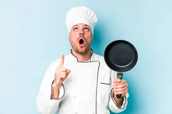 年轻的高加索厨师手持飞行锅 隔离在蓝色背景中 顶部有开口 — 图库照片