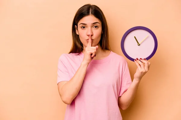 Mujer Hispana Joven Sosteniendo Reloj Aislado Sobre Fondo Beige Guardando — Foto de Stock