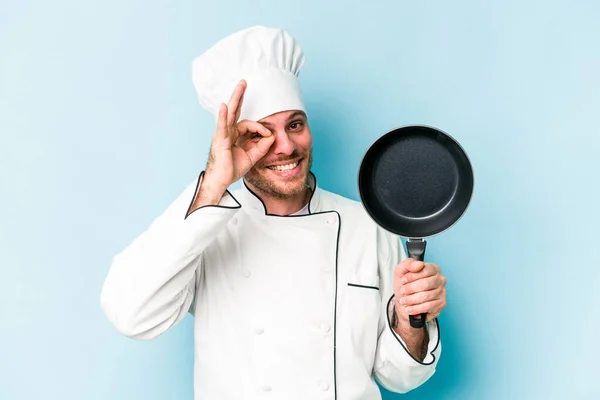 年轻的高加索厨师拿着用蓝色背景隔开的飞盘兴奋地保持着对着眼睛的正常姿势 — 图库照片