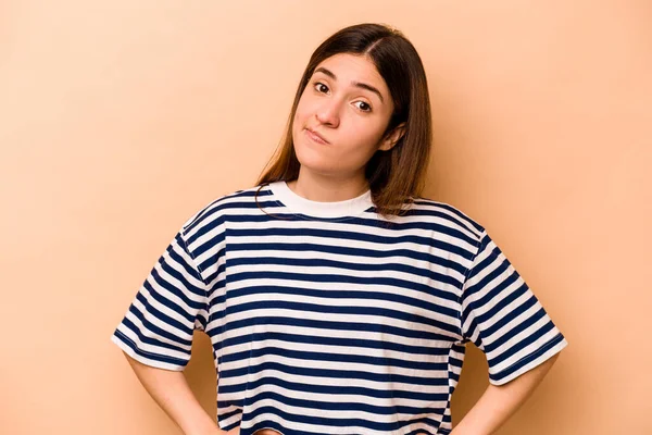 Latin kökenli genç bir kadın bej arka planda izole edilmiş kafası karışmış, şüpheci ve kararsız hissediyor..