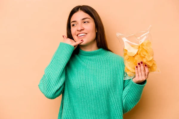 Bej arka planda izole edilmiş bir çanta dolusu çipi tutan İspanyol genç kadın parmaklarıyla bir cep telefonu hareketi gösteriyor..
