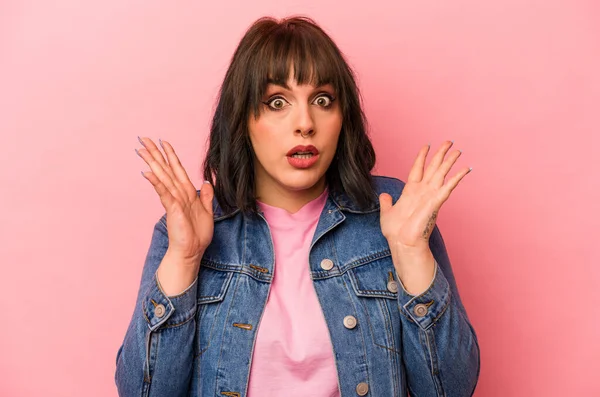 Pembe arka planda izole edilmiş genç beyaz kadın şaşırmış ve şok olmuş..