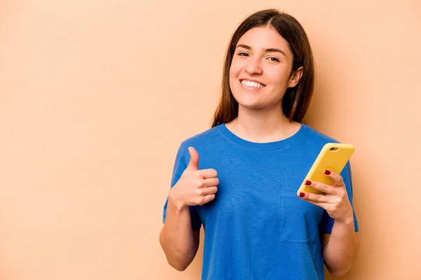 Giovane Donna Caucasica Possesso Cellulare Isolato Sfondo Beige Sorridente Alzando — Foto Stock