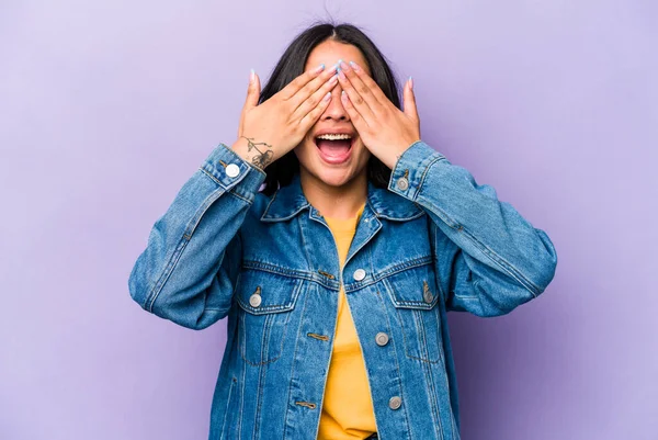 Mor arka planda izole edilmiş genç İspanyol kadın elleriyle gözlerini kapatıyor, geniş bir gülümsemeyle bir sürpriz bekliyor..