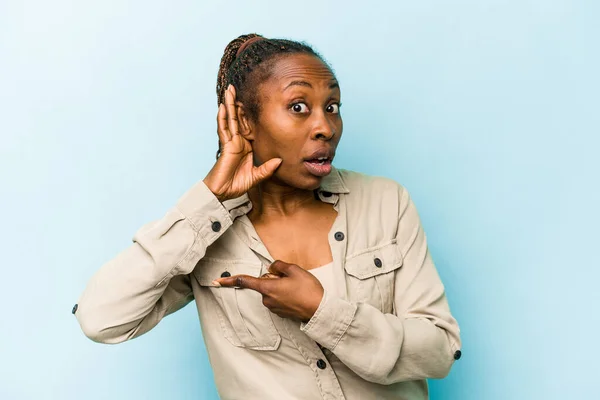 Young african american woman isolated on blue background trying to listening a gossip.